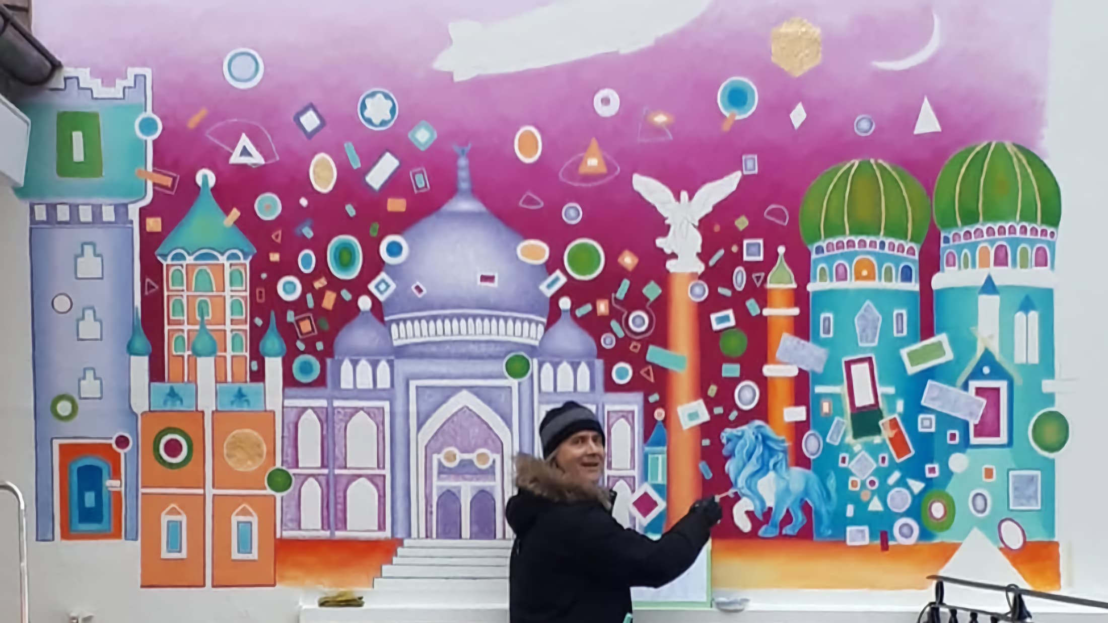 Stefan Eichler vor seiner Wandmalerei mit Kuppeln, Türmen, blauem Löwen und Zeppelin, gemalt für NewBoxes in Ravensburg